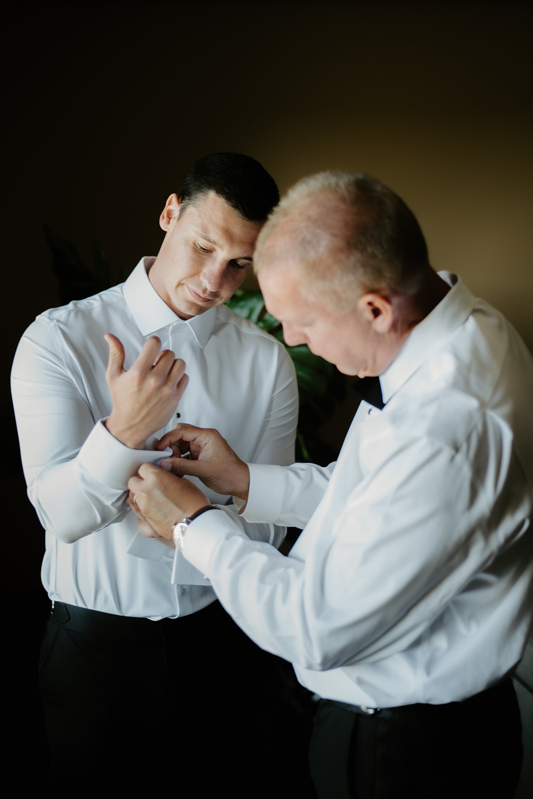 Father helping the groom adjust his cufflinks in a quiet moment of preparation before the wedding.